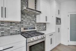 Gourmet kitchen featuring a stainless steel range with a coordinating hood, grey mosaic tile backsplash, white shaker cabinetry with matte black hardware, white countertops, and a built-in microwave - 
