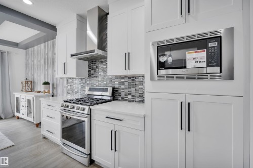 Modern kitchen featuring white cabinetry, stainless steel appliances, a mosaic tile backsplash, quartz countertops, and wood-finish flooring - 3898 Robins Crescent, Edmonton, AB 