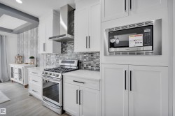 Modern kitchen featuring white cabinetry, stainless steel appliances, a mosaic tile backsplash, quartz countertops, and wood-finish flooring - 
