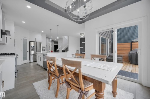 Open-concept dining space featuring a coffered ceiling with a modern chandelier, wood-finish flooring, and direct access to an outdoor deck through sliding glass doors - 3898 Robins Crescent, Edmonton, AB 