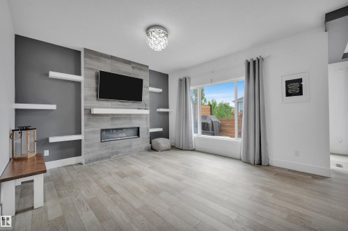 Contemporary living space featuring a tiled fireplace with an integrated electric insert, a mounted television, and floating shelving - 3898 Robins Crescent, Edmonton, AB 
