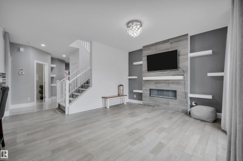 Living area featuring wood-finish flooring, a contemporary tiled fireplace surround with an integrated electric fireplace, and a crystal flush mount ceiling fixture - 3898 Robins Crescent, Edmonton, AB 
