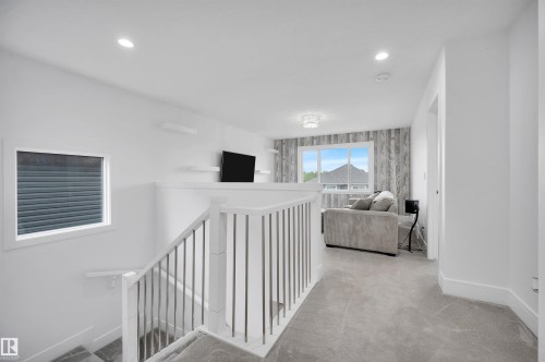 Upper-level loft space featuring light gray carpeting, recessed ceiling lighting, and a window with a neighborhood backdrop - 3898 Robins Crescent, Edmonton, AB 