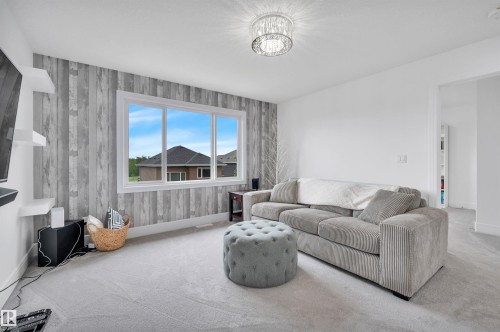 Spacious room featuring light grey carpeting, a large window with white trim, and a decorative accent wall with a wood-look finish - 3898 Robins Crescent, Edmonton, AB 