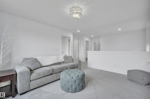 Carpeted room featuring a ceiling-mounted crystal chandelier, recessed lighting, and a white half-wall - 3898 Robins Crescent, Edmonton, AB 