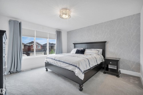 Spacious room featuring a large window, light gray carpeting, and a statement wall with a subtle tree-branch pattern - 3898 Robins Crescent, Edmonton, AB 