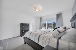 Bedroom featuring light gray carpeting, a crystal-style ceiling light fixture, and a large window with roller shades and gray drapes - 