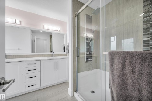 Contemporary bathroom featuring a spacious glass-enclosed shower with multiple spray functions, a dual vanity with white cabinetry and integrated sinks, a large mirror, and tiled flooring - 3898 Robins Crescent, Edmonton, AB 