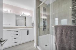 Contemporary bathroom featuring a spacious glass-enclosed shower with multiple spray functions, a dual vanity with white cabinetry and integrated sinks, a large mirror, and tiled flooring - 