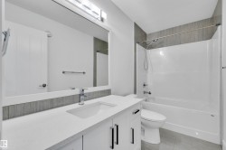 Bathroom featuring a vanity with a white countertop and integrated sink, chrome faucet, and white cabinetry with dark pulls - 