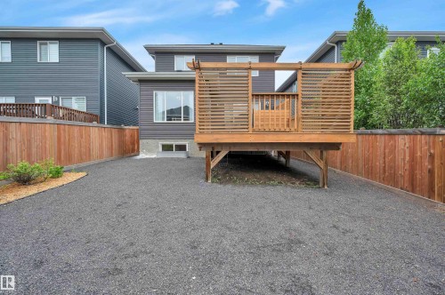Exterior featuring dark grey siding with white trim, a raised wood-finish deck with privacy screens, full-height privacy fencing, and a gravel yard - 3898 Robins Crescent, Edmonton, AB 
