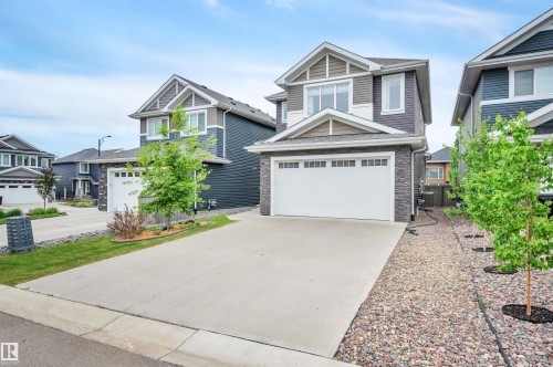Contemporary two-story residence featuring dark siding with lighter accent panels, a stone facade, and a two-car garage with a concrete driveway - 3898 Robins Crescent, Edmonton, AB 
