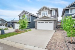 Contemporary two-story residence featuring dark siding with lighter accent panels, a stone facade, and a two-car garage with a concrete driveway - 