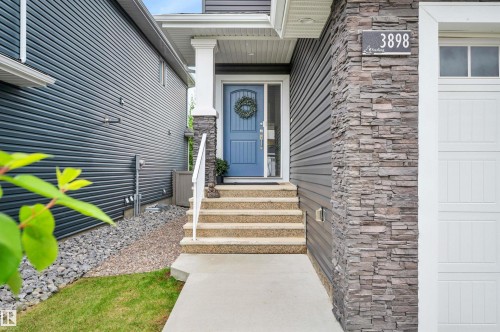 Stone veneer and horizontal siding exterior with a light blue entry door, concrete walkway, and white garage door - 3898 Robins Crescent, Edmonton, AB 
