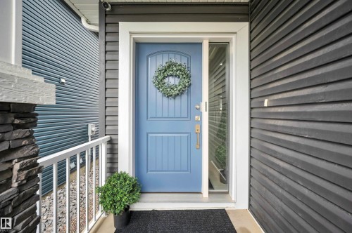 Entryway featuring a blue paneled door with sidelight, dark horizontal siding, and a stone-clad column with white railing - 3898 Robins Crescent, Edmonton, AB 