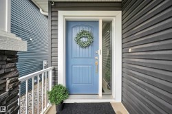 Entryway featuring a blue paneled door with sidelight, dark horizontal siding, and a stone-clad column with white railing - 