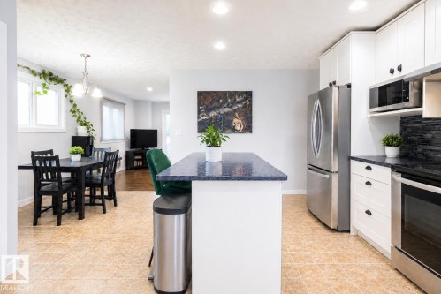 Kitchen featuring white cabinetry, stainless steel appliances, a dark blue speckled countertop, and a tiled backsplash - 17932 93 Avenue, Edmonton, AB 
