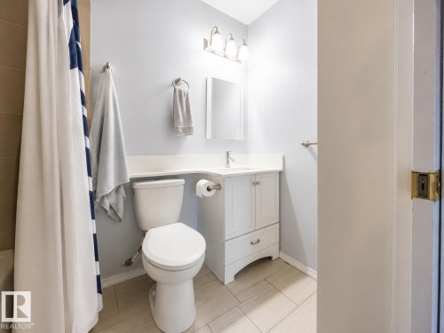 Bathroom featuring a white vanity with built-in sink, coordinating toilet, and light-toned rectangular floor tiles - 17932 93 Avenue, Edmonton, AB 