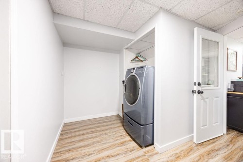 Dedicated laundry area featuring a front-loading washer, elevated pedestal, integrated hanging rod, wood-finish flooring, and a crisp white paneled door with glass insert - 17932 93 Avenue, Edmonton, AB 