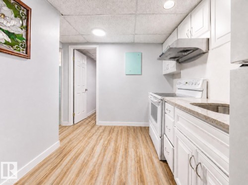 Kitchenette featuring white cabinetry, a stainless steel sink, light-toned countertops, and a white electric range with an overhead stainless steel range hood - 17932 93 Avenue, Edmonton, AB 