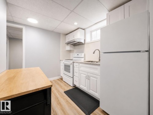 Kitchenette featuring white cabinetry, a white refrigerator, and a white range with an overhead microwave - 17932 93 Avenue, Edmonton, AB 