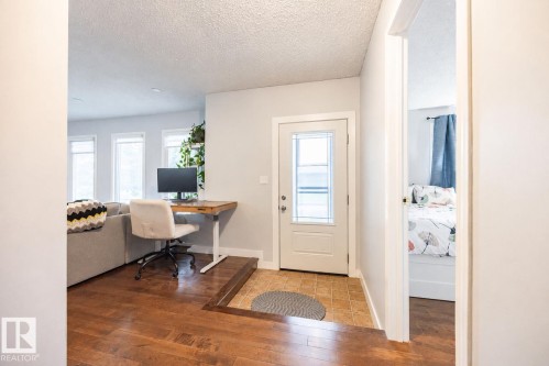 Entryway featuring a white door with decorative glass, tiled flooring, and wood-finish flooring in the adjacent living area - 17932 93 Avenue, Edmonton, AB 