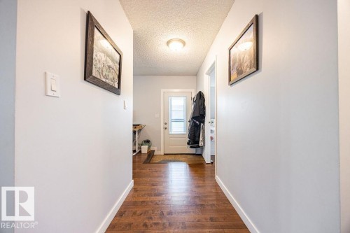 Hallway featuring wood-finish flooring, light-colored walls, white baseboards, and a semi-flush ceiling light fixture - 17932 93 Avenue, Edmonton, AB 