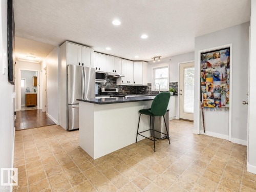Modern kitchen featuring white cabinetry, stainless steel appliances, dark countertops, a dark tile backsplash, and light-toned tile flooring - 17932 93 Avenue, Edmonton, AB 