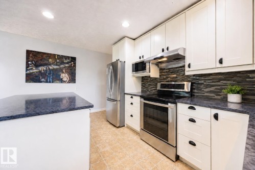 Kitchen featuring stainless steel appliances, white cabinetry, dark countertops, a mosaic tile backsplash, and light-toned floor tiling - 17932 93 Avenue, Edmonton, AB 