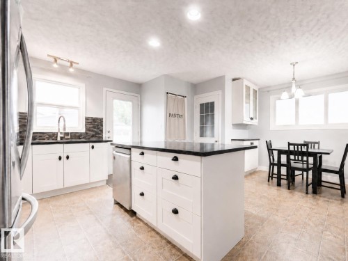 Spacious kitchen featuring a central island with integrated storage, white shaker-style cabinetry, dark countertops, and tile flooring - 17932 93 Avenue, Edmonton, AB 