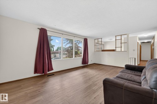 Spacious living area featuring expansive windows, wood-finish flooring, and a decorative room divider - 13920 64 Street, Edmonton, AB 