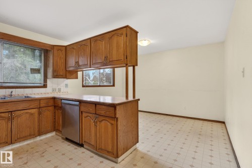 Kitchen featuring wood cabinetry, stainless steel dishwasher, corner sink, and tiled flooring - 13920 64 Street, Edmonton, AB 