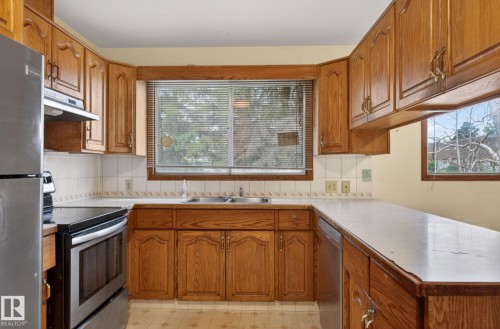 Kitchen featuring extensive wood cabinetry with decorative paneling, white countertop surfaces, and a tile backsplash - 13920 64 Street, Edmonton, AB 