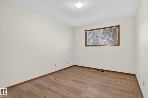Room featuring wood-finish flooring, neutral wall paint, and a window with a wood trim - 13920 64 Street, Edmonton, AB 