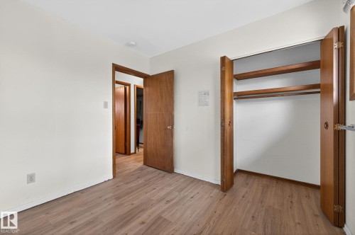 Room featuring wood-finish flooring, white painted walls, a built-in closet with bifold doors, and wooden interior doors - 13920 64 Street, Edmonton, AB 