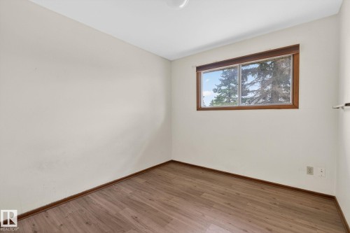 Light-filled room featuring wood-finish flooring, neutral wall paint, white ceiling, and a large window with wood trim - 13920 64 Street, Edmonton, AB 