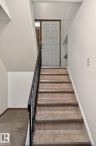 Staircase featuring tile treads, a black metal handrail, and a paneled door - 13920 64 Street, Edmonton, AB 