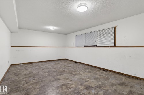 Spacious room featuring wood-finish flooring, white walls with a chair rail, and multiple windows with horizontal blinds - 13920 64 Street, Edmonton, AB 