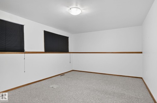 Room featuring light gray carpeting, crisp white walls, brown wood trim, and two windows with black horizontal blinds - 13920 64 Street, Edmonton, AB 
