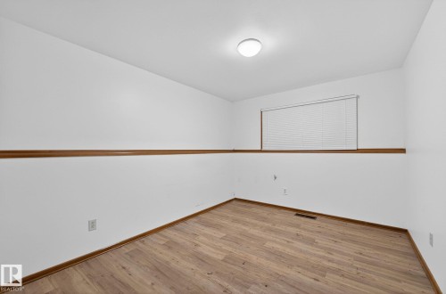 Room featuring wood-finish flooring, crisp white walls, and a recessed window with blinds - 13920 64 Street, Edmonton, AB 