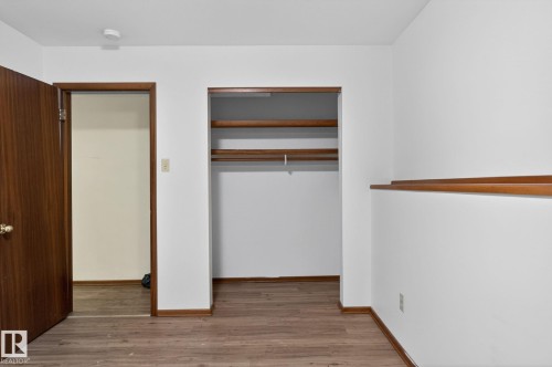 Room with wood-finish flooring, white walls, and a built-in closet featuring shelving and a hanging rod - 13920 64 Street, Edmonton, AB 