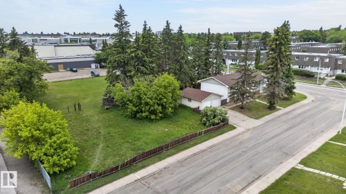 Expansive corner lot featuring a residential structure with a detached garage, mature trees, a wooden perimeter fence, and a paved street - 13920 64 Street, Edmonton, AB 