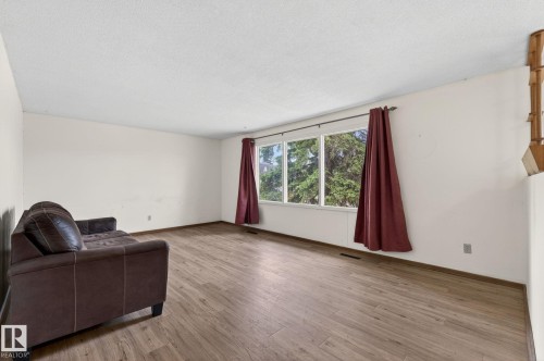 Spacious room featuring wood-finish flooring, white walls, and a large multi-pane window - 13920 64 Street, Edmonton, AB 