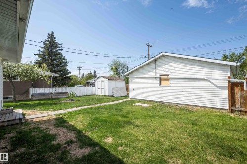 Expansive rear yard featuring green lawn, a detached white vinyl-sided garage, a white shed, and a privacy fence - 4414 54 Avenue, Barrhead, AB - Outdoor