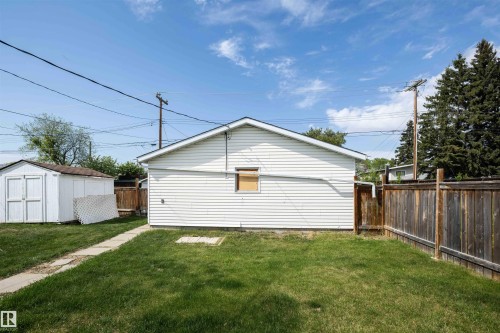 Expansive backyard with a manicured lawn, concrete pathway, white vinyl-sided structure, and a wooden privacy fence - 4414 54 Avenue, Barrhead, AB - Outdoor