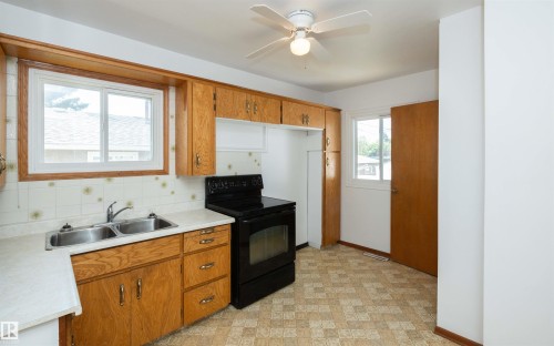 Kitchen featuring wood-finish cabinetry, a double basin stainless steel sink, a black electric range, and patterned flooring - 4414 54 Avenue, Barrhead, AB - Indoor Photo Showing Kitchen With Double Sink