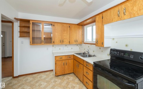 Kitchen featuring wood cabinetry, white countertops, a dual basin stainless steel sink, and a black electric range - 4414 54 Avenue, Barrhead, AB - Indoor Photo Showing Kitchen With Double Sink