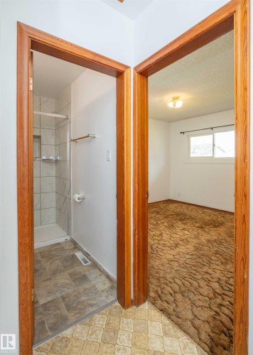 Tiled flooring in a bathroom entryway featuring a shower stall with white subway tile and built-in shelving - 4414 54 Avenue, Barrhead, AB - Indoor