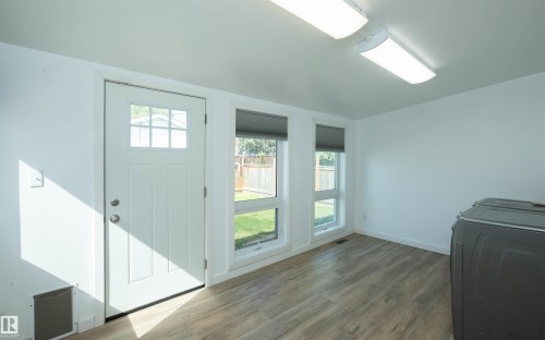 Interior space featuring wood-finish flooring, two large windows with roller shades, and a rear exit door with an integrated multi-pane window - 4414 54 Avenue, Barrhead, AB - Indoor Photo Showing Other Room