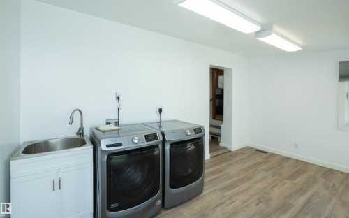 Dedicated laundry space featuring wood-finish flooring, a utility sink with white cabinetry, and overhead fluorescent lighting - 4414 54 Avenue, Barrhead, AB - Indoor Photo Showing Laundry Room